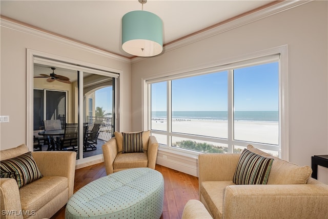 living room featuring hardwood / wood-style flooring, a beach view, ceiling fan, ornamental molding, and a water view