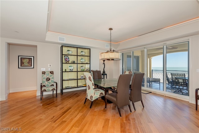 dining room with hardwood / wood-style flooring, a tray ceiling, crown molding, and a water view