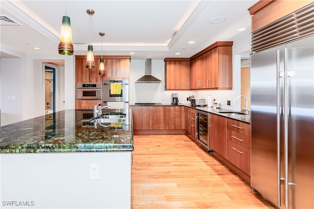 kitchen featuring sink, beverage cooler, hanging light fixtures, wall chimney range hood, and appliances with stainless steel finishes