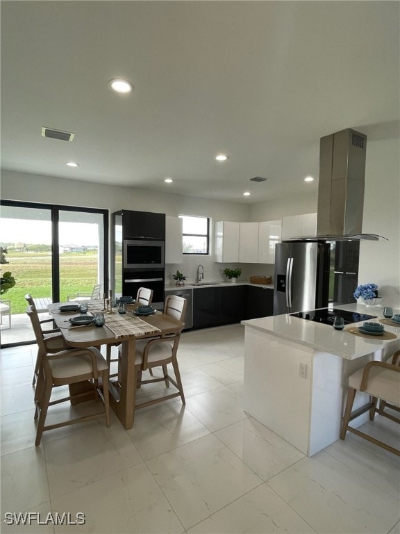 kitchen with white cabinetry, sink, stainless steel appliances, island exhaust hood, and a breakfast bar area