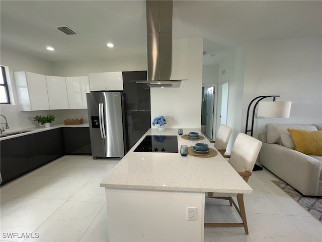 kitchen featuring stainless steel refrigerator with ice dispenser, black electric stovetop, island range hood, sink, and white cabinetry