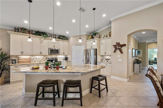 kitchen featuring an island with sink, appliances with stainless steel finishes, pendant lighting, and a kitchen breakfast bar