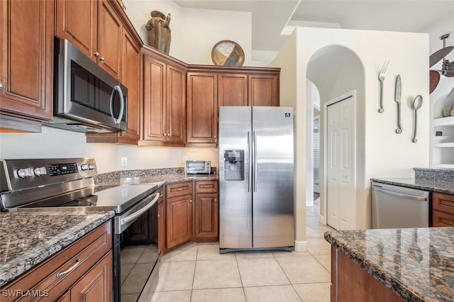 kitchen with dark stone countertops, appliances with stainless steel finishes, and light tile patterned floors