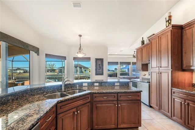 kitchen featuring decorative light fixtures, sink, light tile patterned floors, and dark stone counters