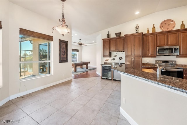 kitchen with light tile patterned flooring, appliances with stainless steel finishes, dark stone countertops, beverage cooler, and hanging light fixtures