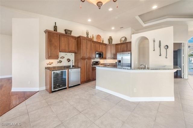 kitchen with stone counters, a kitchen island with sink, stainless steel appliances, wine cooler, and light tile patterned flooring