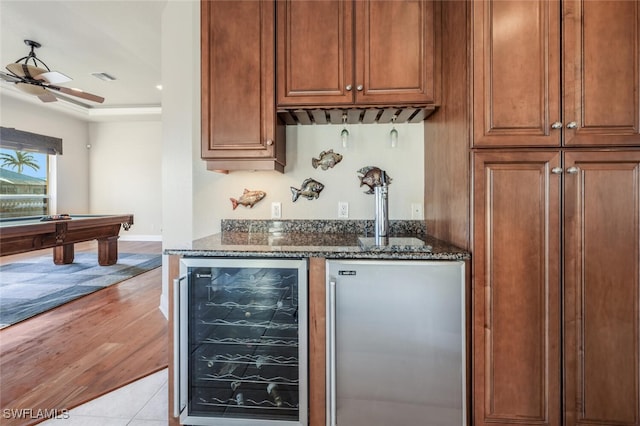 bar featuring light tile patterned flooring, stainless steel built in refrigerator, beverage cooler, dark stone counters, and ceiling fan