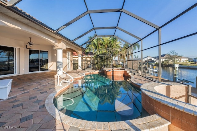 view of swimming pool with an in ground hot tub, ceiling fan, glass enclosure, a water view, and a patio area