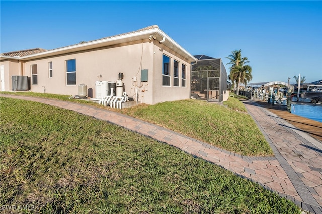 rear view of property featuring cooling unit, a lanai, and a lawn