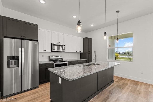 kitchen featuring sink, stainless steel appliances, light stone counters, light hardwood / wood-style flooring, and decorative light fixtures