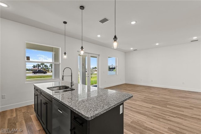 kitchen featuring dishwasher, sink, light stone counters, light hardwood / wood-style flooring, and a center island with sink