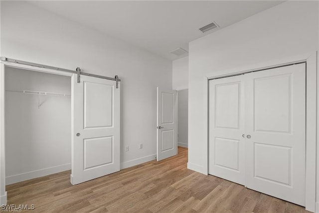 unfurnished bedroom featuring a barn door, a closet, and light wood-type flooring