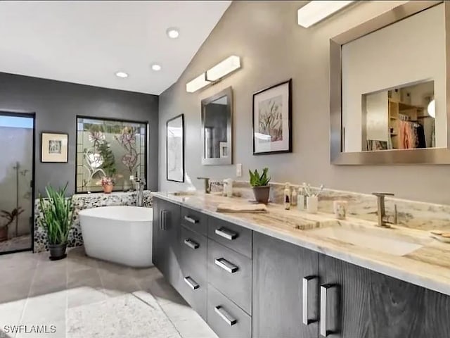 bathroom with tile patterned flooring, vanity, a bath, and vaulted ceiling