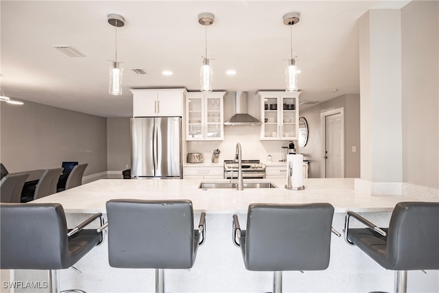 kitchen with pendant lighting, wall chimney range hood, stainless steel fridge, a kitchen bar, and white cabinetry