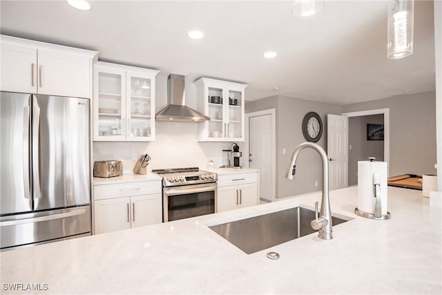 kitchen with stainless steel appliances, sink, wall chimney range hood, pendant lighting, and white cabinetry