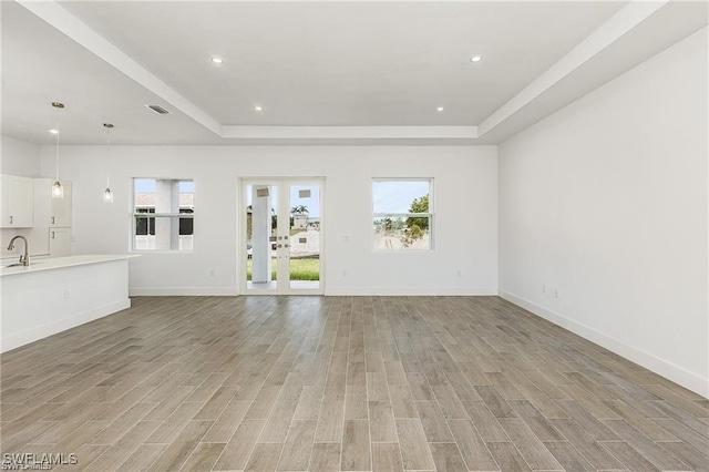 unfurnished living room with light hardwood / wood-style floors, a tray ceiling, and sink