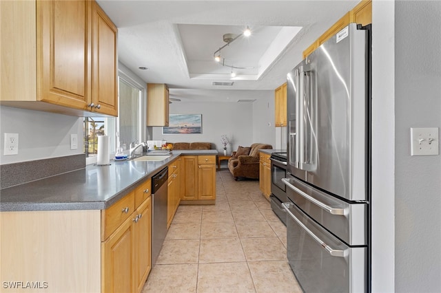 kitchen with kitchen peninsula, stainless steel appliances, a tray ceiling, sink, and light tile patterned flooring