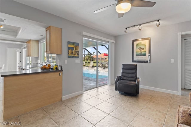 living area featuring rail lighting, a tray ceiling, ceiling fan, sink, and light tile patterned floors