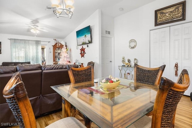 dining room featuring ceiling fan with notable chandelier, light hardwood / wood-style flooring, and vaulted ceiling