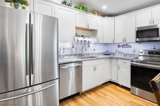 kitchen with light stone countertops, appliances with stainless steel finishes, light wood-type flooring, sink, and white cabinetry