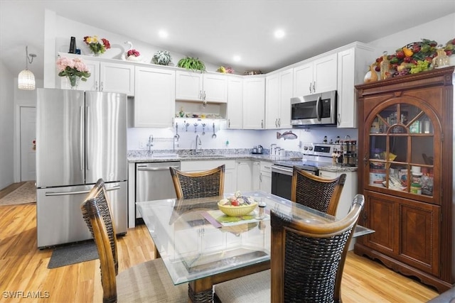 kitchen with white cabinetry, sink, stainless steel appliances, lofted ceiling, and light wood-type flooring