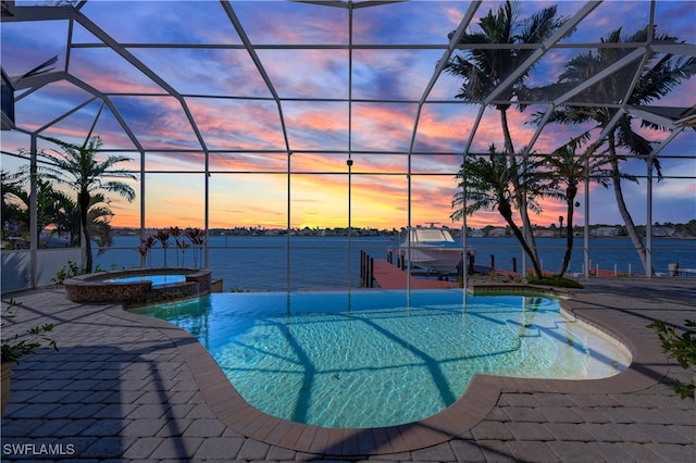 pool at dusk featuring glass enclosure, a water view, and an in ground hot tub