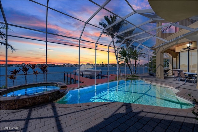 pool at dusk featuring an in ground hot tub, a dock, a water view, and ceiling fan