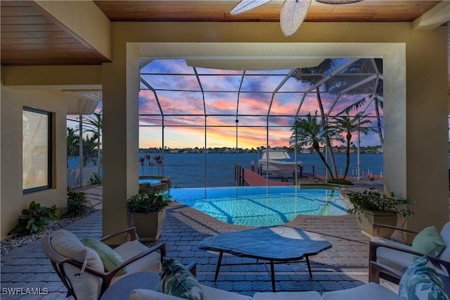 patio terrace at dusk featuring a water view, ceiling fan, and a lanai