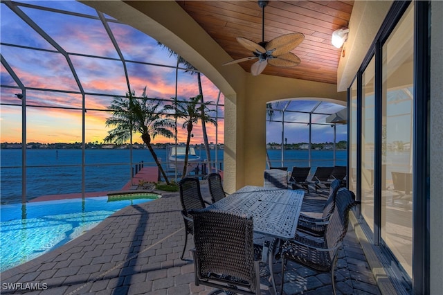 patio terrace at dusk with a lanai, ceiling fan, and a water view