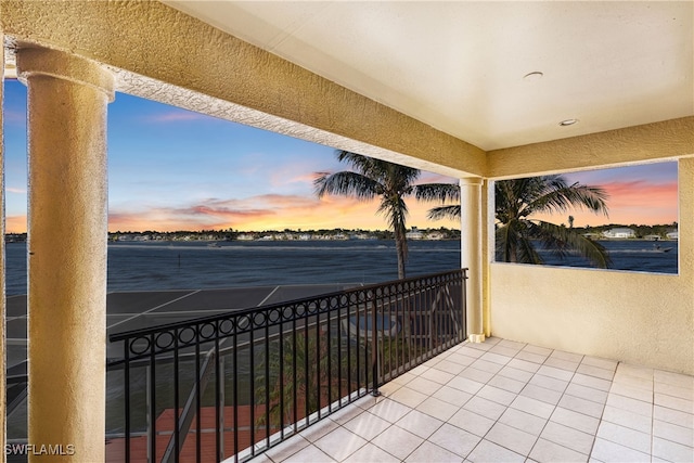 balcony at dusk featuring a water view