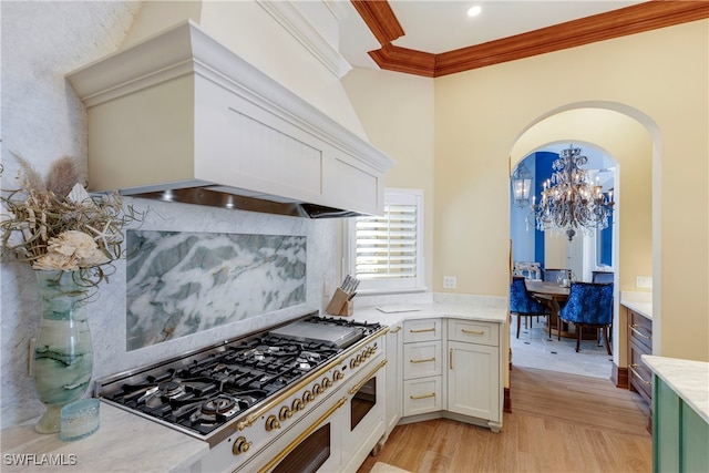 kitchen with premium range hood, white cabinets, light hardwood / wood-style flooring, ornamental molding, and a chandelier