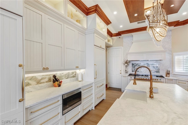 kitchen featuring light wood-type flooring, light stone counters, ornamental molding, stainless steel appliances, and hanging light fixtures