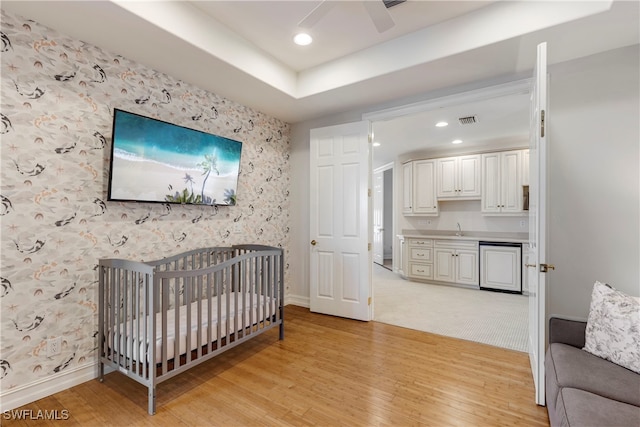 bedroom featuring ceiling fan, a crib, sink, and light hardwood / wood-style flooring