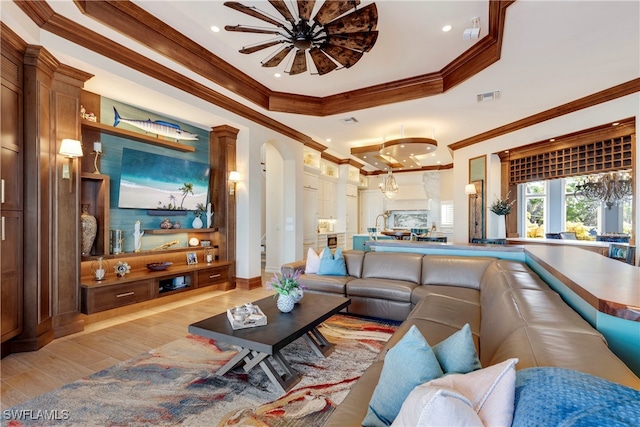 living room featuring light wood-type flooring, a raised ceiling, ceiling fan, and ornamental molding