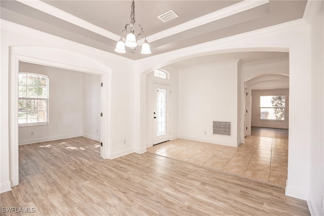 spare room with a tray ceiling, crown molding, an inviting chandelier, and light wood-type flooring