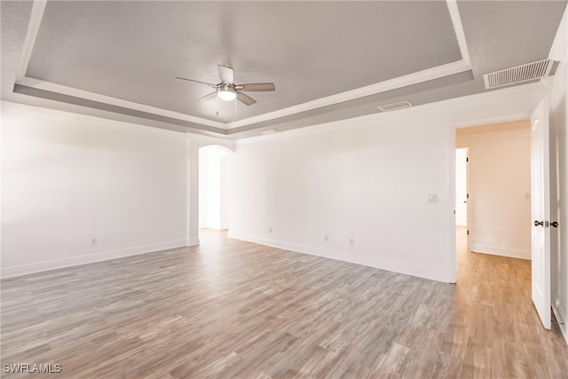 empty room with a tray ceiling, light hardwood / wood-style flooring, and ceiling fan