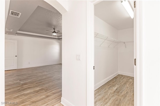 walk in closet featuring a tray ceiling, ceiling fan, and light wood-type flooring