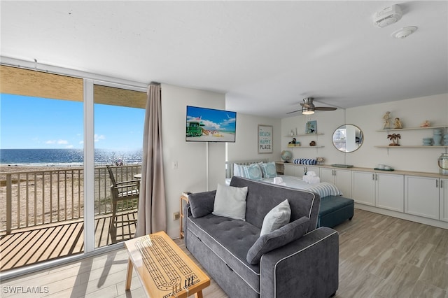 living room featuring a water view, ceiling fan, a beach view, light hardwood / wood-style floors, and a wall of windows