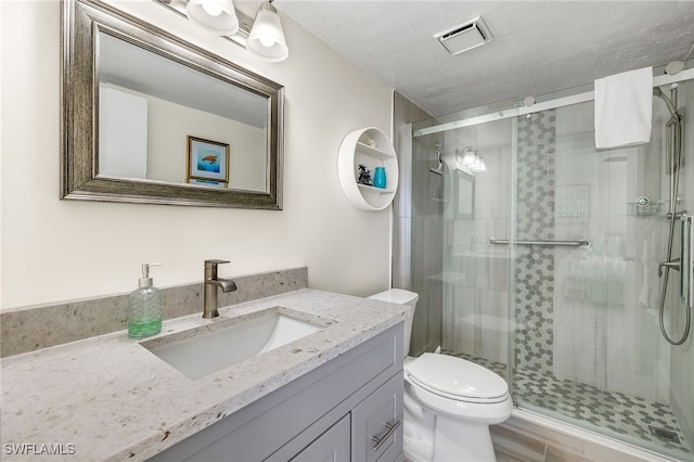 bathroom with a shower with door, vanity, a textured ceiling, and toilet