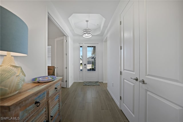 hallway featuring dark hardwood / wood-style floors, a tray ceiling, and a notable chandelier