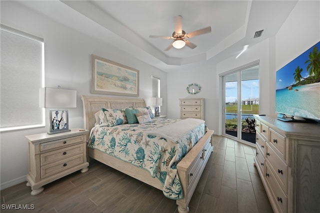 bedroom with access to outside, ceiling fan, dark hardwood / wood-style flooring, and a tray ceiling