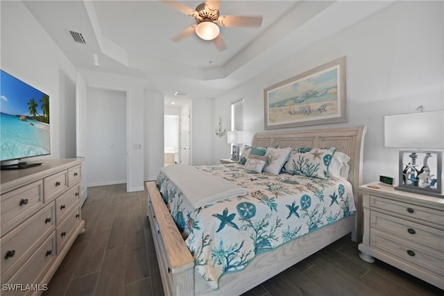 bedroom featuring a raised ceiling, dark hardwood / wood-style floors, ensuite bath, and ceiling fan