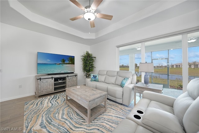 living room with ceiling fan, a raised ceiling, and wood-type flooring