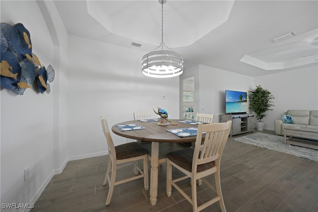 dining room featuring dark hardwood / wood-style flooring, a raised ceiling, and a notable chandelier