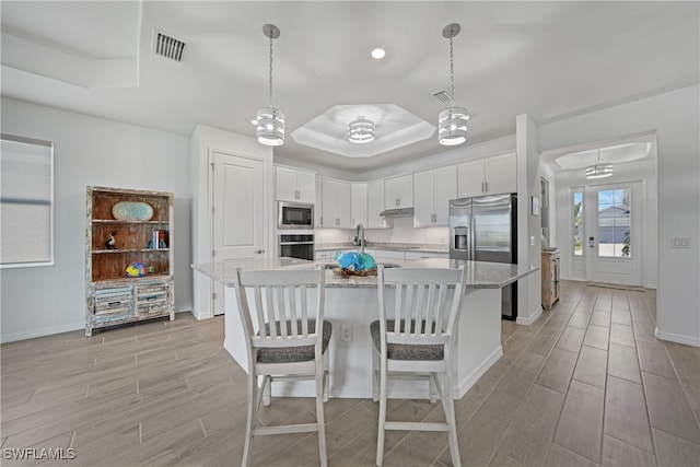 kitchen featuring pendant lighting, white cabinets, a center island with sink, a raised ceiling, and appliances with stainless steel finishes