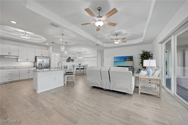 living room with a raised ceiling, ceiling fan, light hardwood / wood-style flooring, and sink