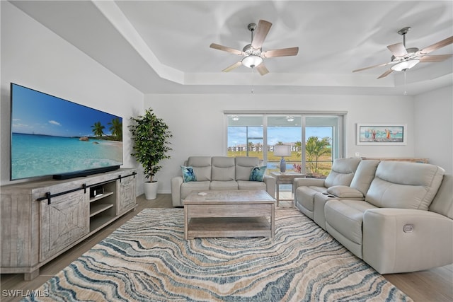 living room with hardwood / wood-style flooring, a raised ceiling, and ceiling fan