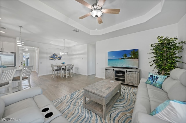 living room with a tray ceiling, ceiling fan, and light wood-type flooring