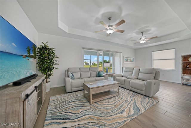 living room with ceiling fan, light wood-type flooring, and a tray ceiling