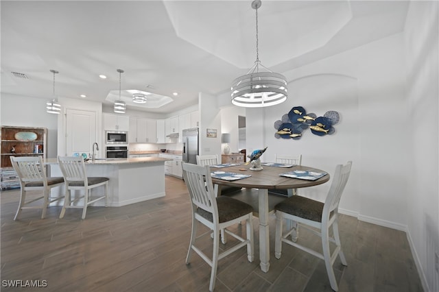 dining room featuring a tray ceiling, dark hardwood / wood-style flooring, a chandelier, and sink